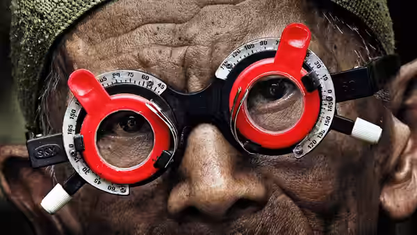 An elderly man wears red trial frame glasses during an exam