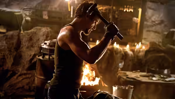 Tony Stark (Robert Downey Jr.) swinging a hammer in a fiery cave workshop