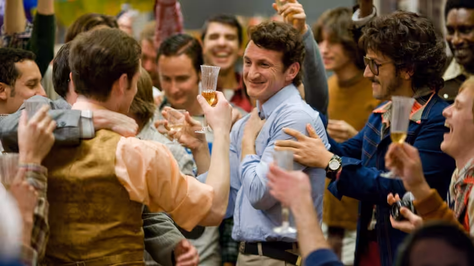 Men at a crowded indoor party raising champagne glasses in celebration