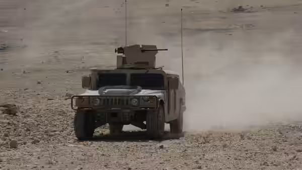 An armoured military vehicle drives across a dusty desert terrain
