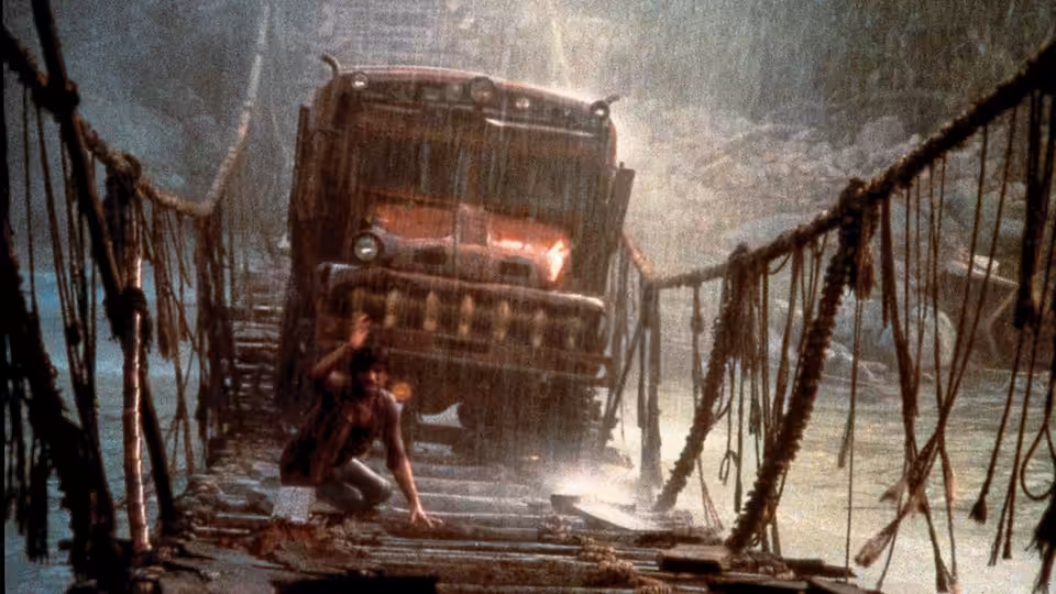 A man braces against a rope bridge as a loaded truck lurches through spray