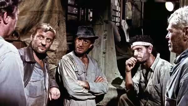 Four men in work clothes confer inside a dim industrial room