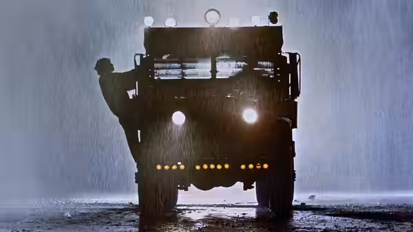 A truck with blazing headlights drives through heavy rain