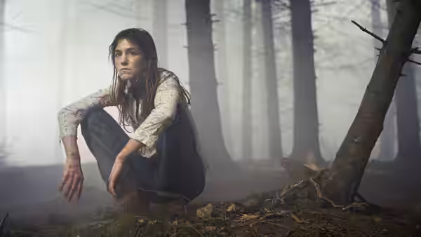 She (Charlotte Gainsbourg) crouching in a misty forest with bloodied hands