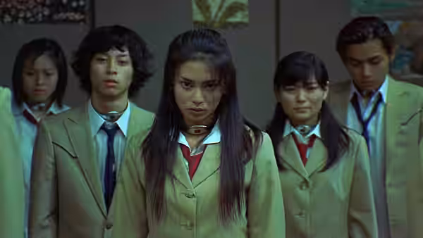 Group of students in beige uniforms stand together looking forward seriously
