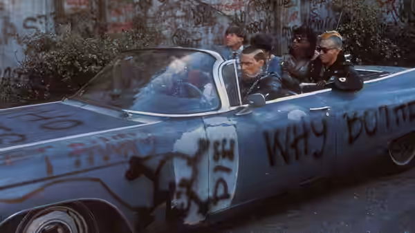 Punks ride in a graffiti-covered convertible along a city street