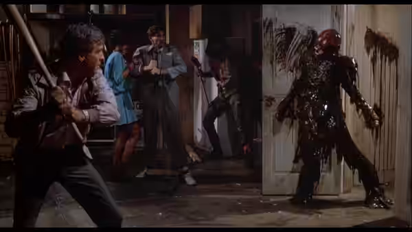 Burt braces with a weapon as friends confront a bloodied corpse in a doorway
