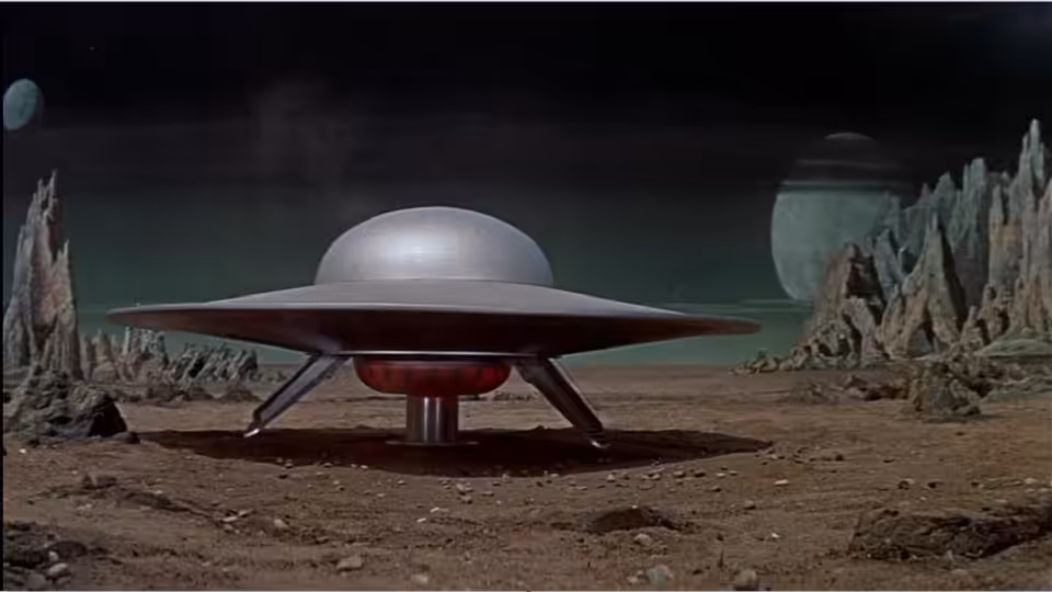 A disc-shaped spacecraft rests on a barren alien landscape between towering rock formations