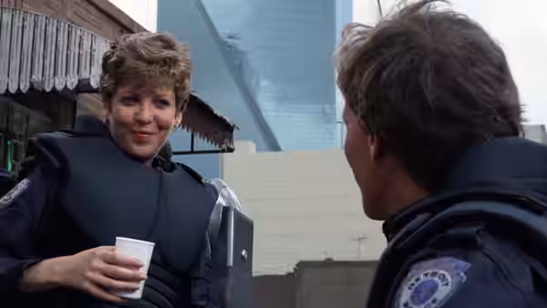 Officer Anne Lewis (Nancy Allen) smiling while holding a cup outdoors