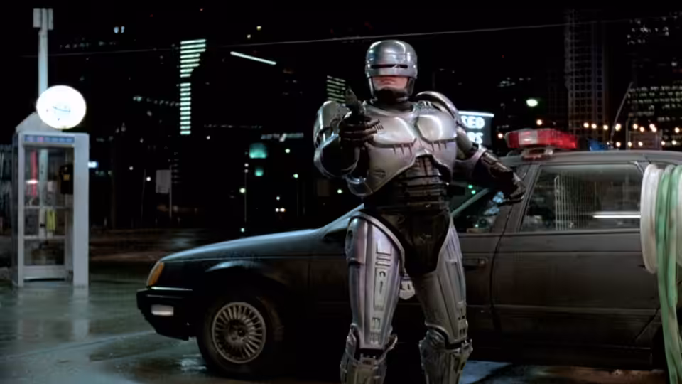 RoboCop (Peter Weller) aiming his gun beside a police car at night