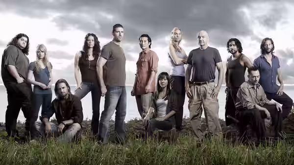 Cast members posing on a grassy hillside overlooking the ocean under cloudy skies