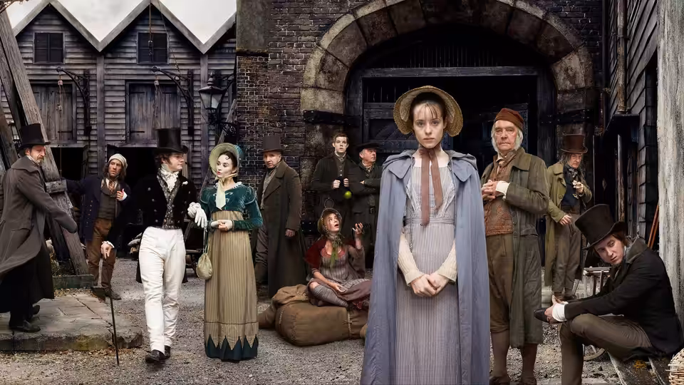 Amy Dorrit (Claire Foy) standing with clasped hands before a group in period dress