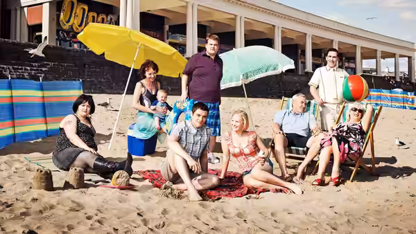 A group of adults and a baby relax together on a sunny beach with umbrellas
