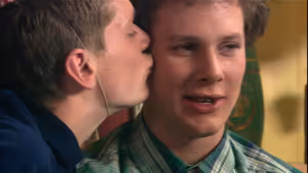 Young man whispering into another man's ear during close conversation