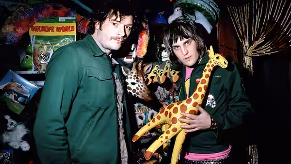 Howard Moon (Julian Barratt) and Vince Noir (Noel Fielding) holding toy giraffes in a cluttered room