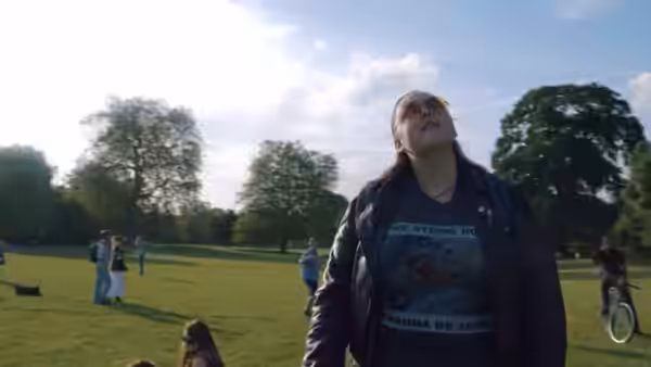 Rachel 'Rae' Earl (Sharon Rooney) stands in a sunny park among other people