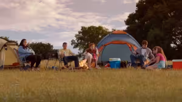 A group of friends sit around a campfire beside their tents