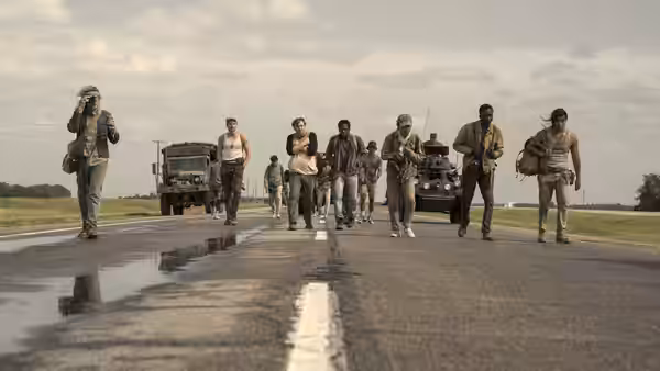 A group of young men walking along a paved road with military trucks following