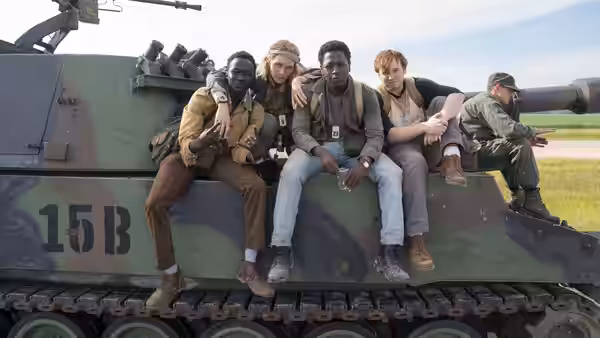 Four young men sitting casually on the turret of a military tank in a field