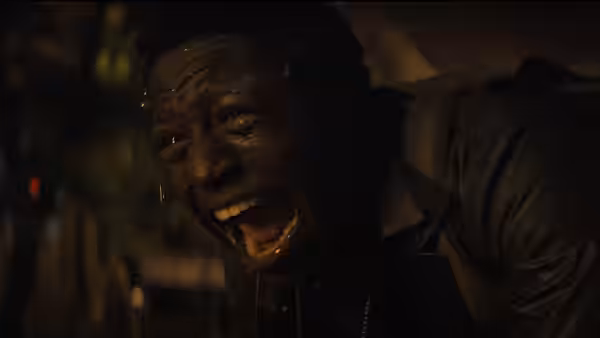 A young man with sweat on his face shouting intensely in the dark