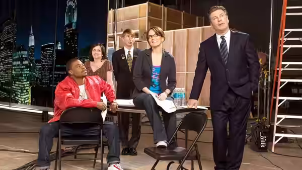 Jack Donaghy stands in a studio while Tracy Jordan sits nearby at a table