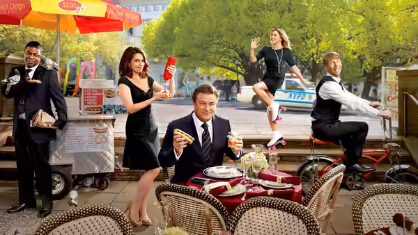 Jack Donaghy eats pizza at an outdoor table as colleagues gather around