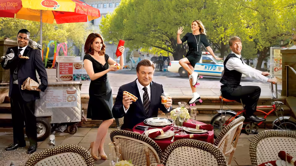 Jack Donaghy eats pizza at an outdoor table as colleagues gather around