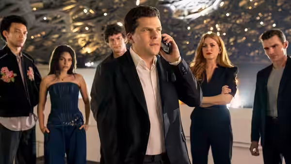 A man speaks on his phone while four others stand around him indoors