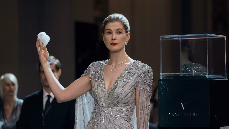 Veronika Vanderberg (Rosamund Pike) raising a white cube beside a glass display case