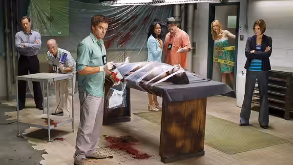 Dexter Morgan (Michael C. Hall) examines a wrapped body on a metal table while colleagues watch in the lab