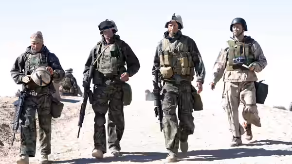 Four soldiers in camouflage walk along a sandy desert path
