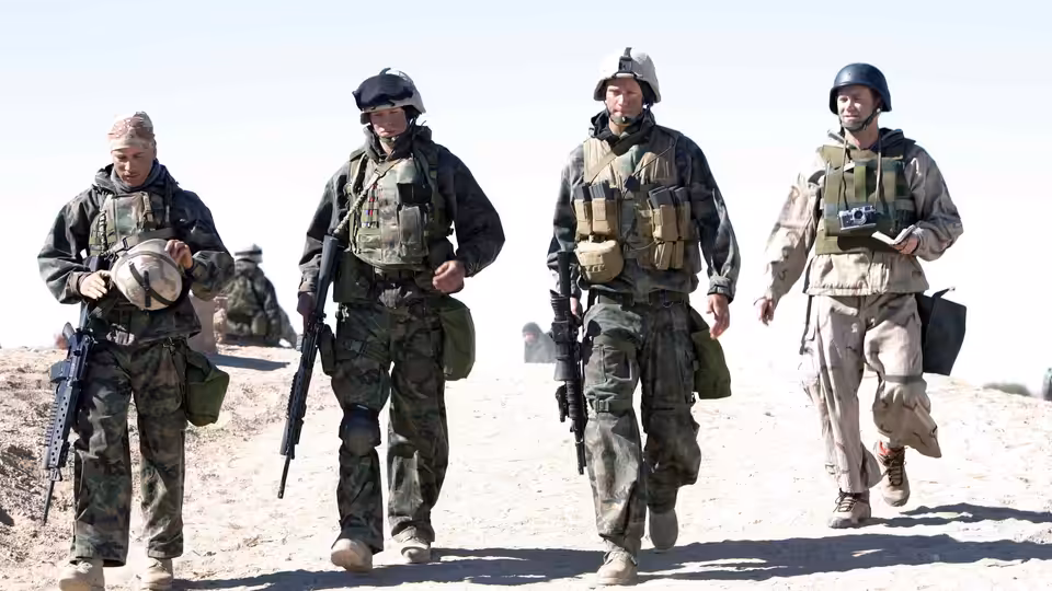 Four soldiers in camouflage walk along a sandy desert path