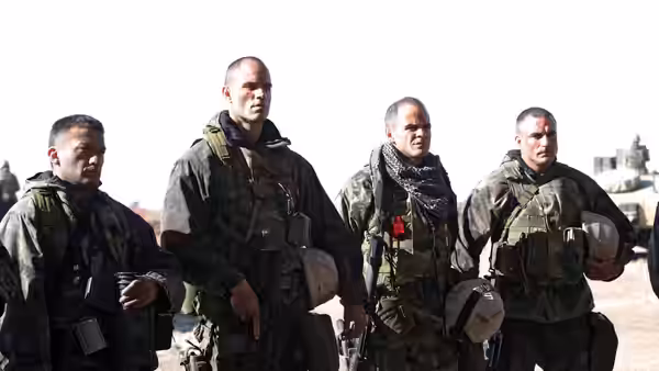 Four soldiers stand together in desert near armored vehicles