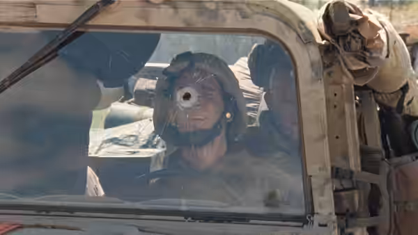 Soldier with head wound sits inside a bullet-damaged vehicle