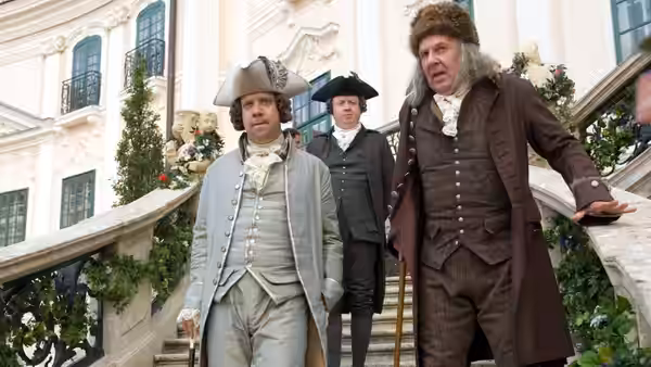 John Adams (Paul Giamatti) and Benjamin Franklin (Tom Wilkinson) descending stairs outside a palace