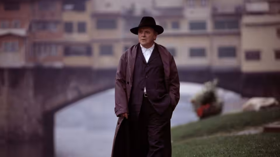 Inspector Renaldo Pazzi (Giancarlo Giannini) stands in a long coat beside the river