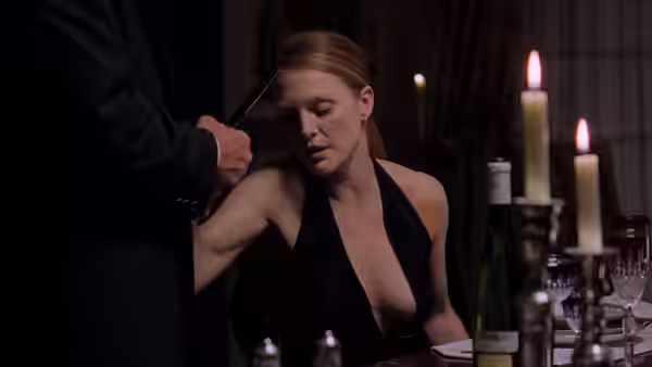 Clarice Starling (Julianne Moore) slumps at a candlelit dining table as a man stands beside her