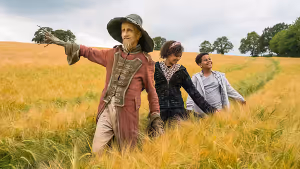 Worzel (Mackenzie Crook) leads two children through a golden field