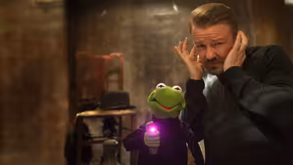 Kermit holds a glowing device beside Dominic Badguy, who covers his ears
