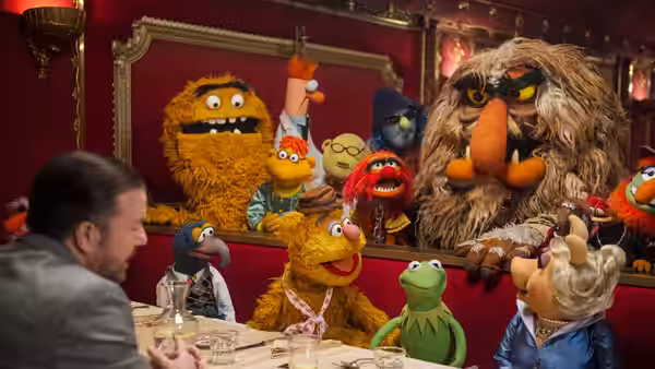 Kermit and the Muppets sit at a banquet table with a man in a suit