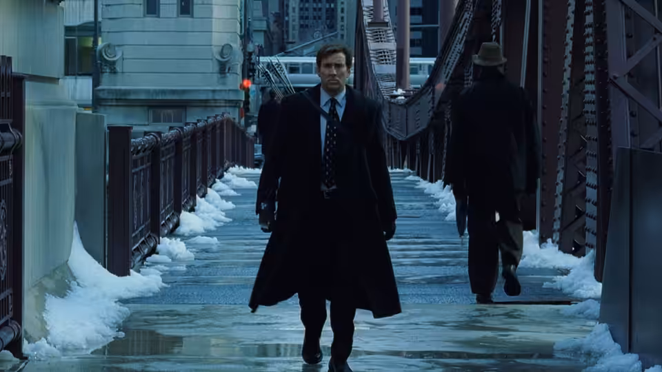 David Spritz (Nicolas Cage) walks across a snow-covered pedestrian bridge in a long coat