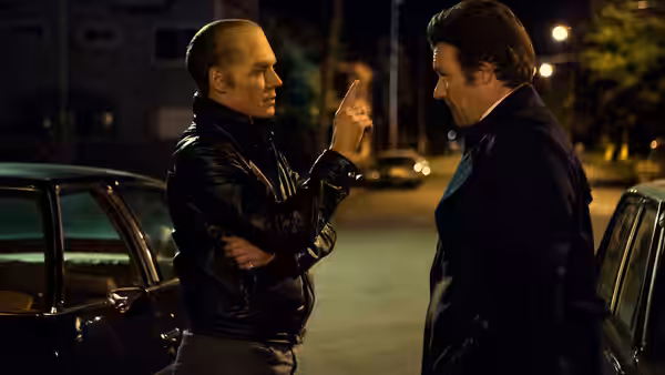 Whitey Bulger (Johnny Depp) raises a finger while speaking to John Connolly (Joel Edgerton) beside parked cars