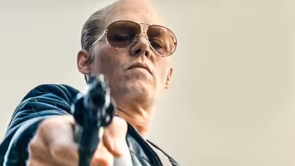 Whitey Bulger (Johnny Depp) points a handgun toward someone offscreen