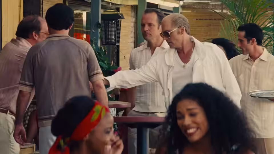 Whitey Bulger (Johnny Depp) reaches across a table at an outdoor gathering