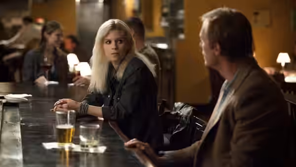 A blonde woman and a man sit facing each other at a bar