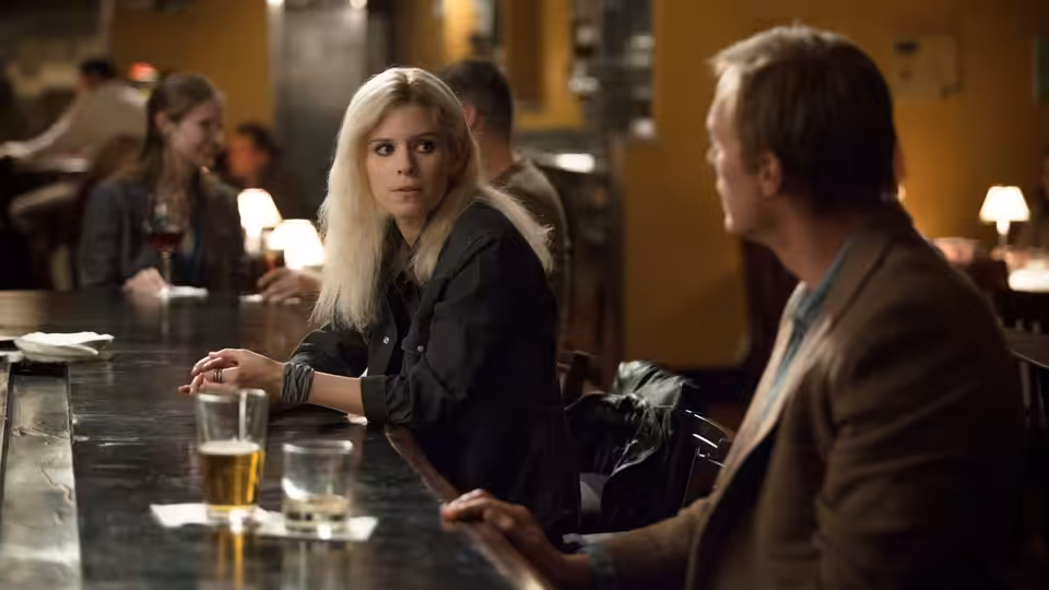 A blonde woman and a man sit facing each other at a bar