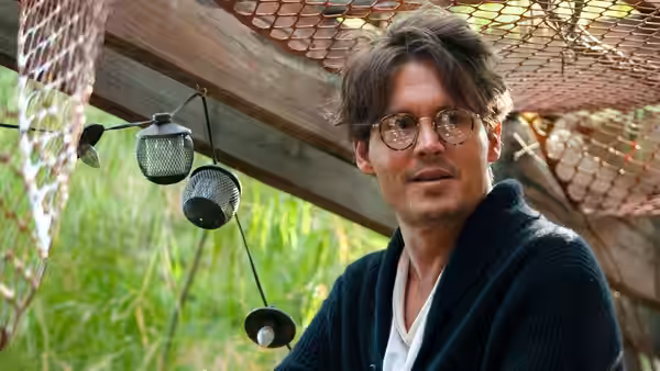 Will Caster (Johnny Depp) sits beneath a mesh canopy outdoors