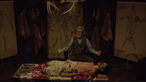 Howard Howe (Michael Parks) gestures beside Wallace Bryton, who lies bloodied on an operating table