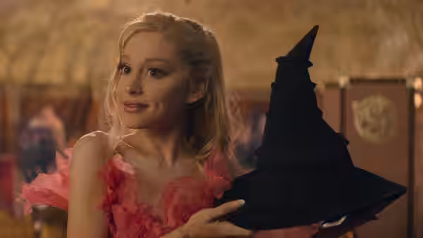 Galinda (Ariana Grande) smiling while holding a black pointed hat