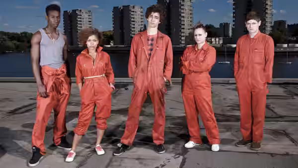 five young adults in red jumpsuits posing on a paved waterfront